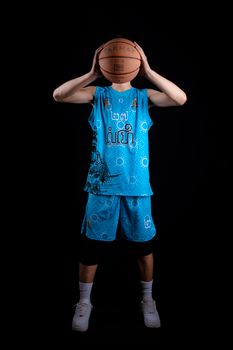 Teenage boy in a blue sports jersey holding a basketball against a black background.