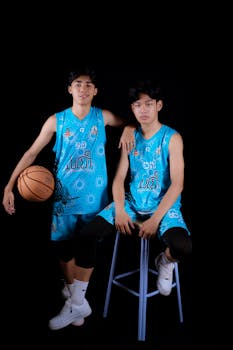 Two young male basketball players in blue sportswear posing against a black studio background.