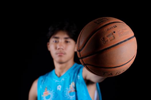 Focused teen basketball player holding a ball with a black background.