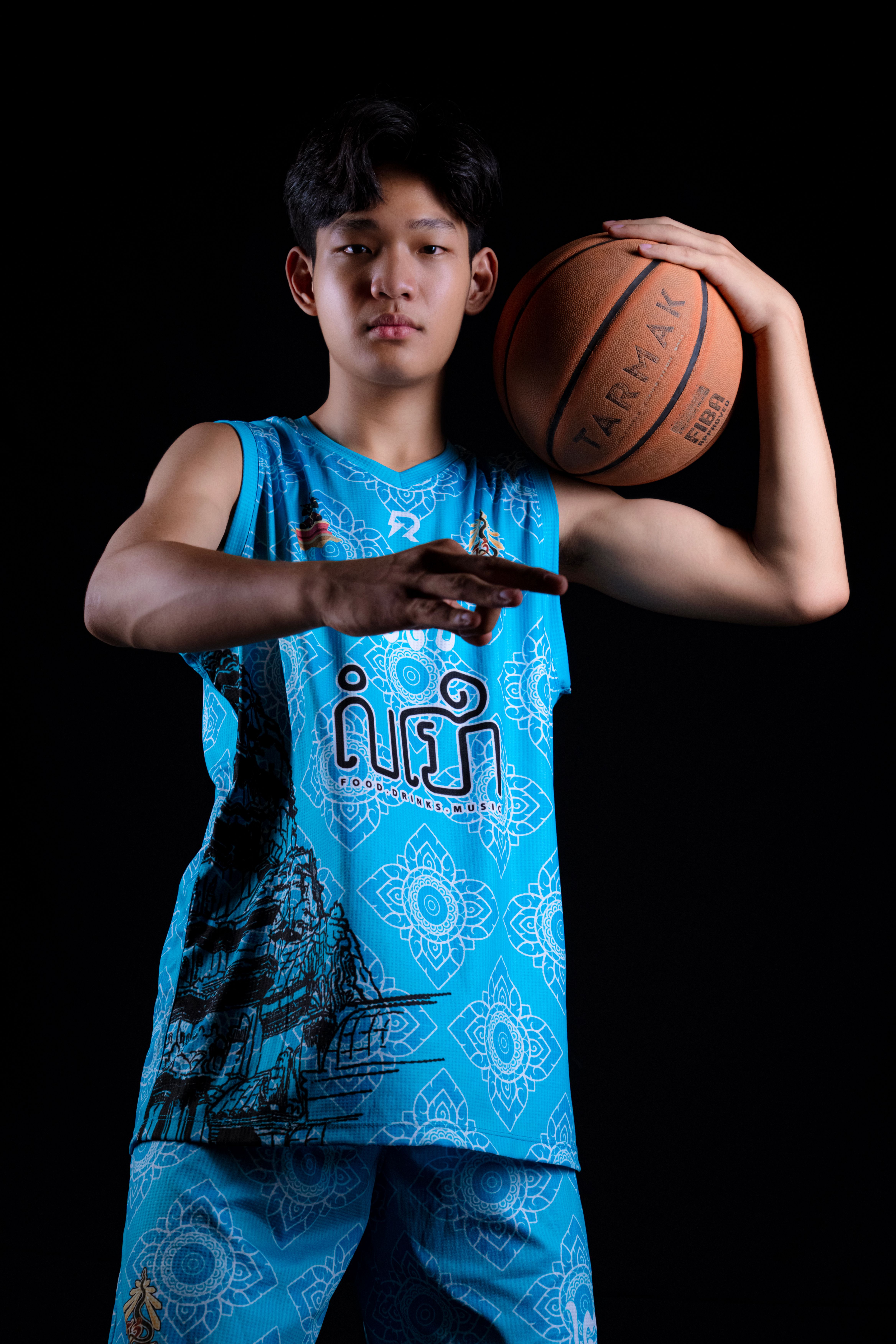 Studio portrait of a young athlete holding a basketball, dressed in blue sportswear on black background.
