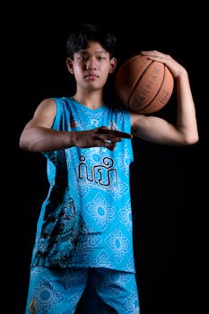 Studio portrait of a young athlete holding a basketball, dressed in blue sportswear on black background.