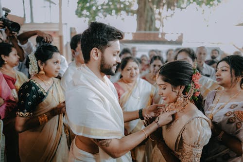 A man in traditional attire is putting a necklace on a woman