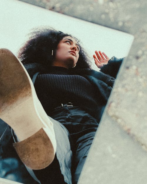 A woman with curly hair and black boots is sitting on the ground