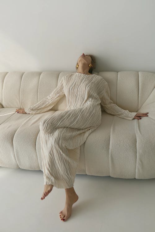 Free Studio Shot of a Woman in a White Dress Sitting on a Sofa Stock Photo