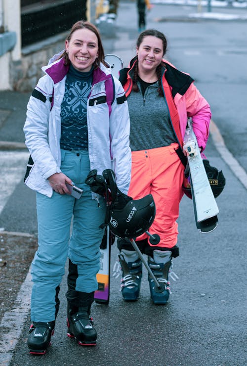 Two women are standing on the street with skis