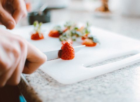 Close-up of fresh strawberries being sliced on a chopping board, perfect for food and kitchen stock images.