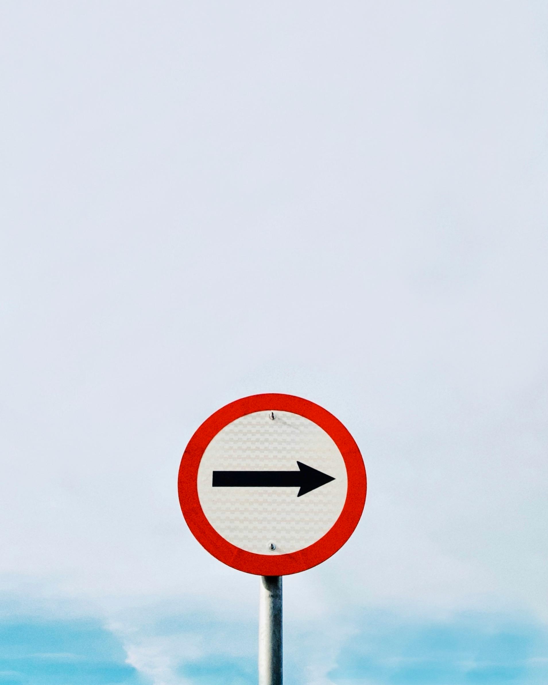 Minimalist shot of a directional street sign on a pole against a clear blue sky.