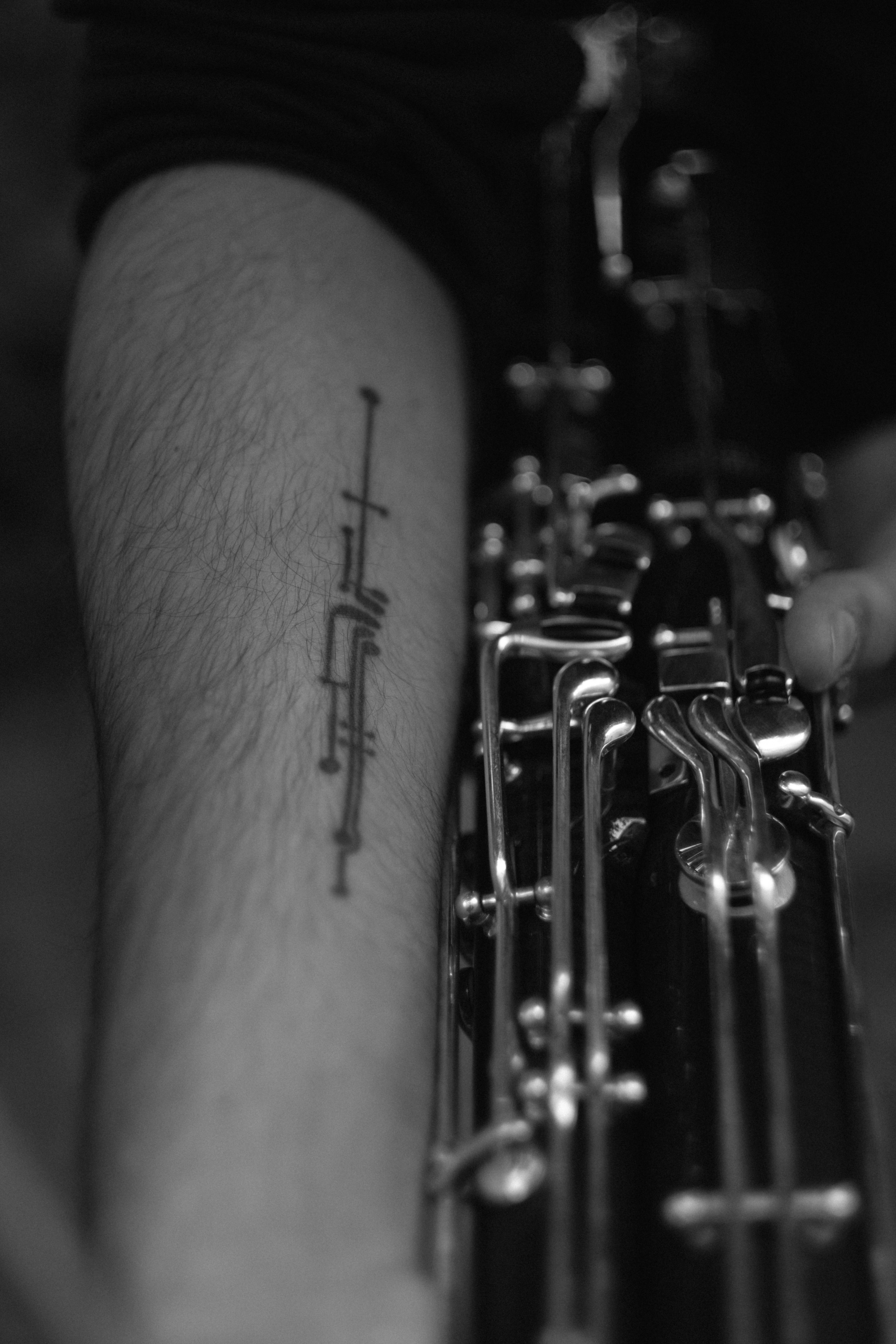 Black and white close-up of a clarinet with a tattooed arm, showing intricate details.