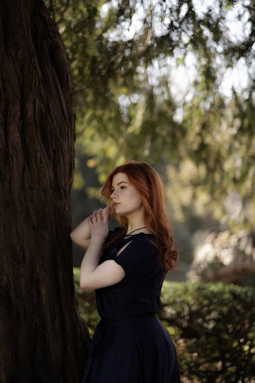 A woman in a dress leaning against a tree