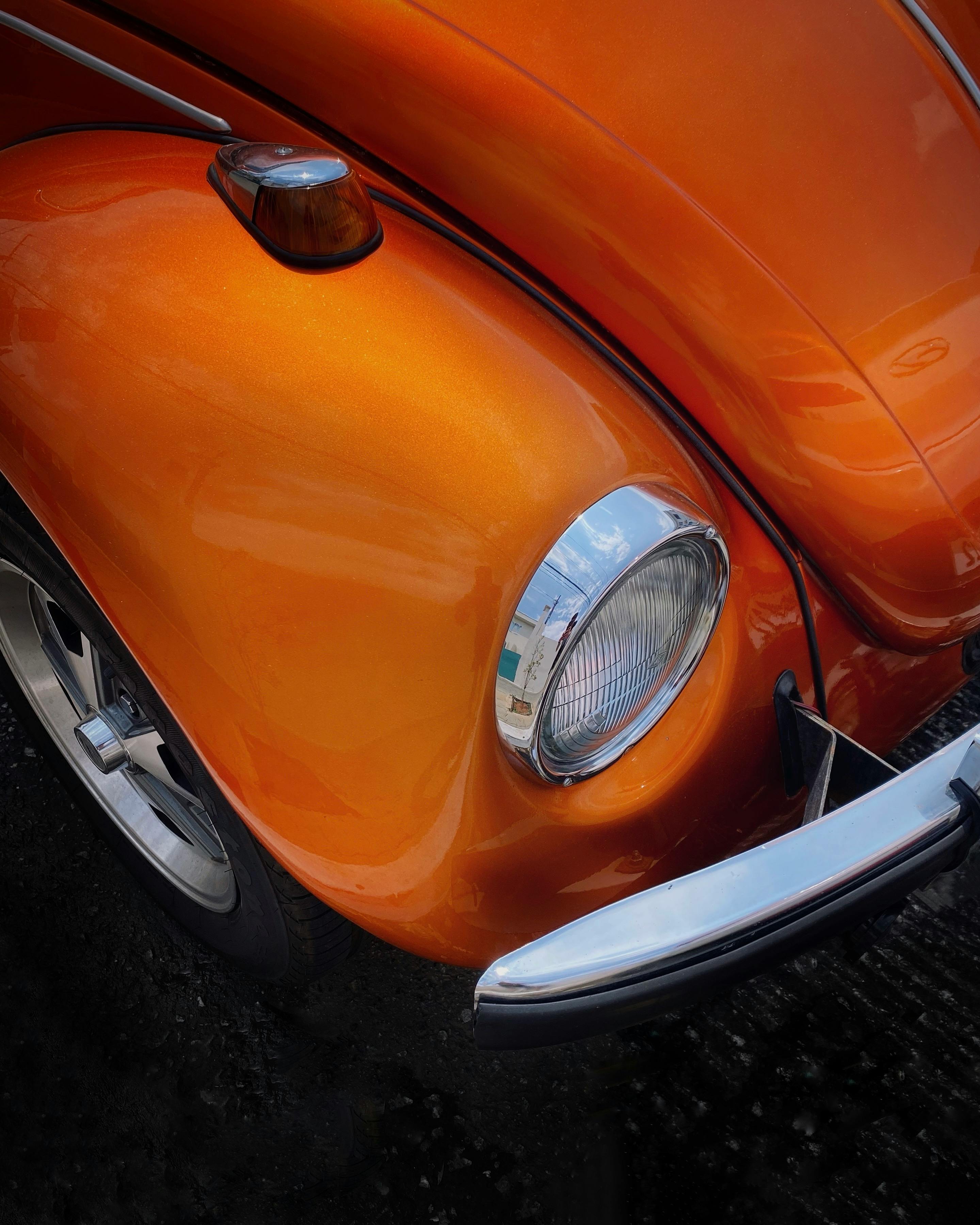 Close-up of a retro orange car featuring shiny chrome and vintage design elements.