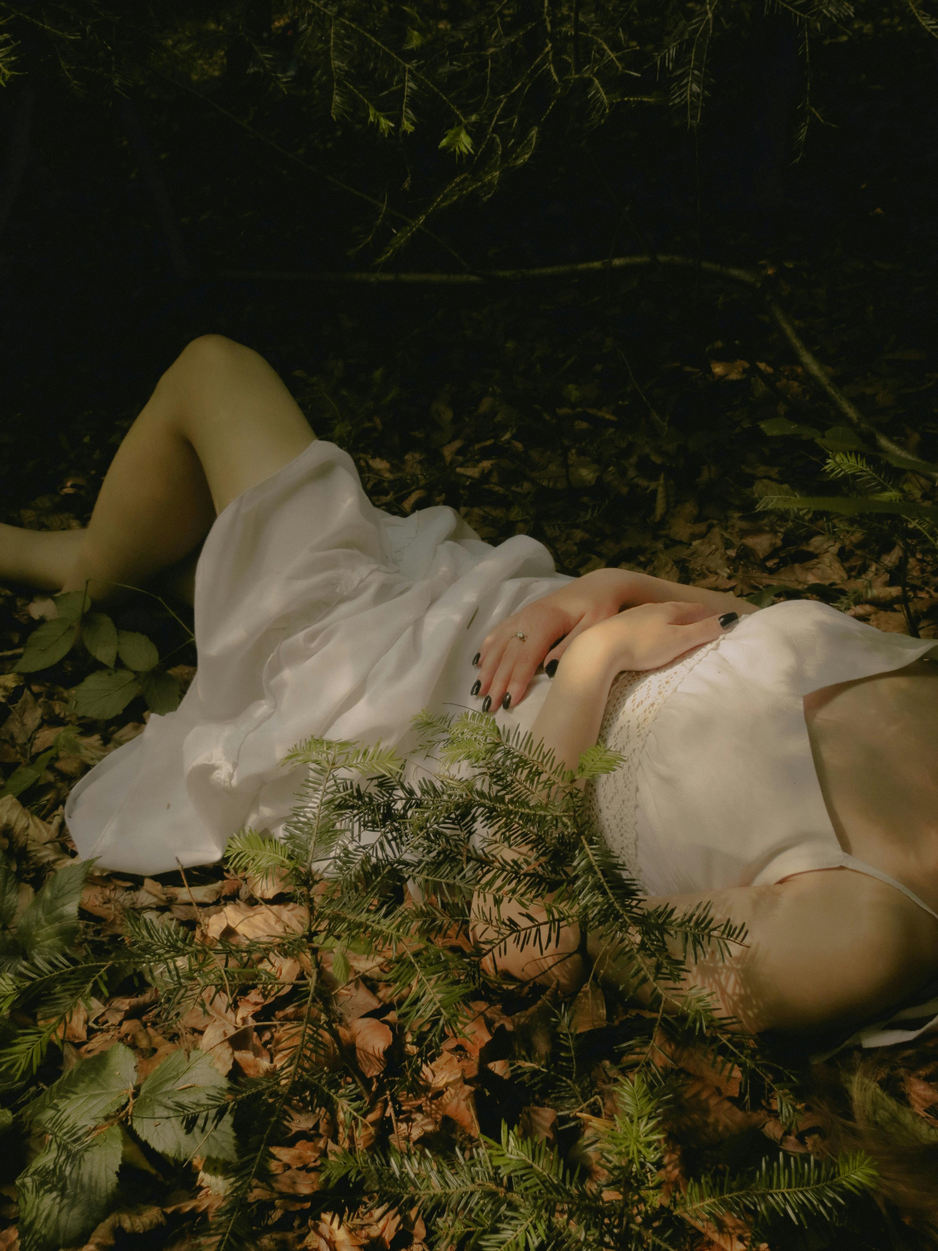 A serene scene of a woman in a white dress lying amid lush forest foliage, exuding tranquility and natural beauty.