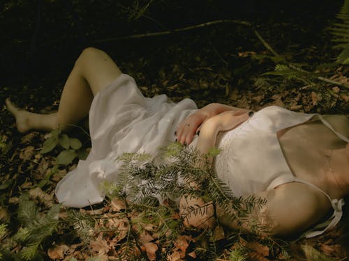 A woman laying down in the woods with leaves