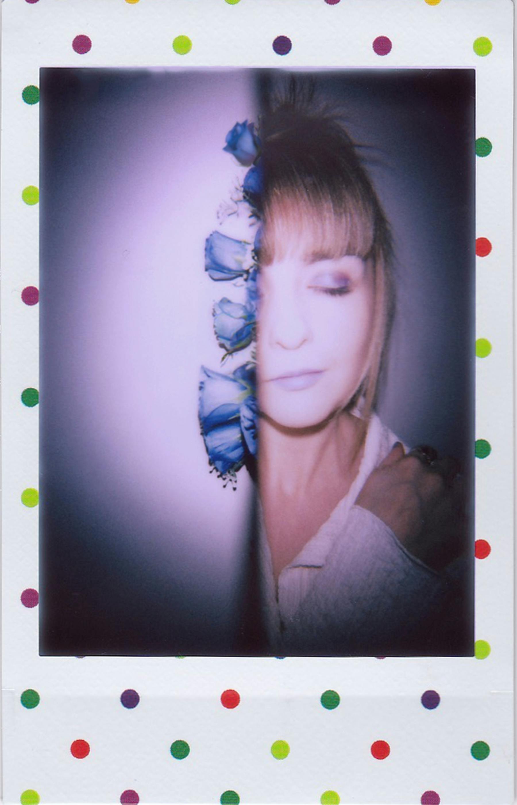 A creative portrait featuring a woman with blue flowers and closed eyes in a polaroid frame.