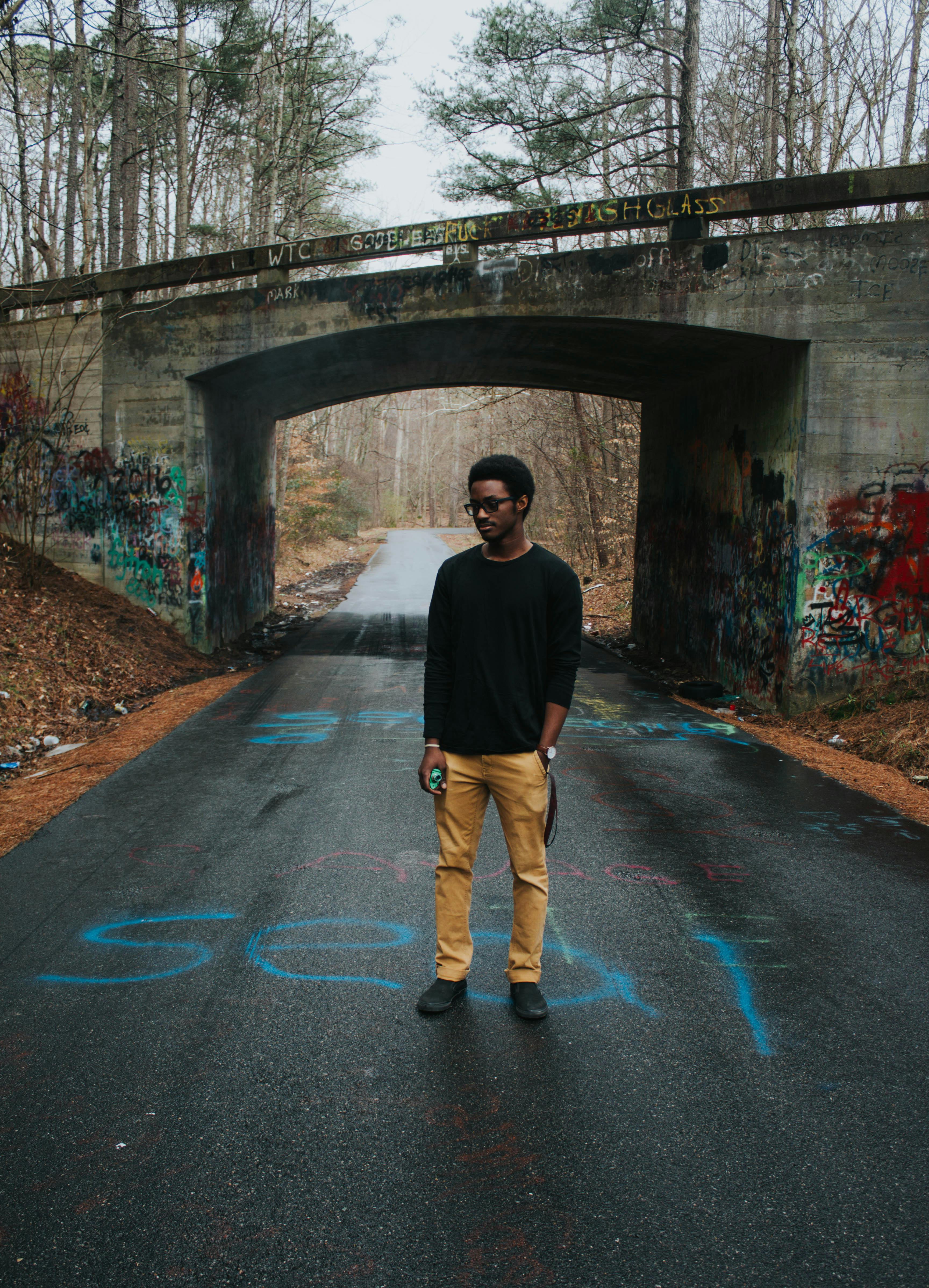 一名男子站在涂鸦覆盖的桥下道路上，展现着城市的生活方式与时尚