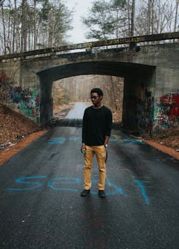 一名男子站在涂鸦覆盖的桥下道路上，展现着城市的生活方式与时尚