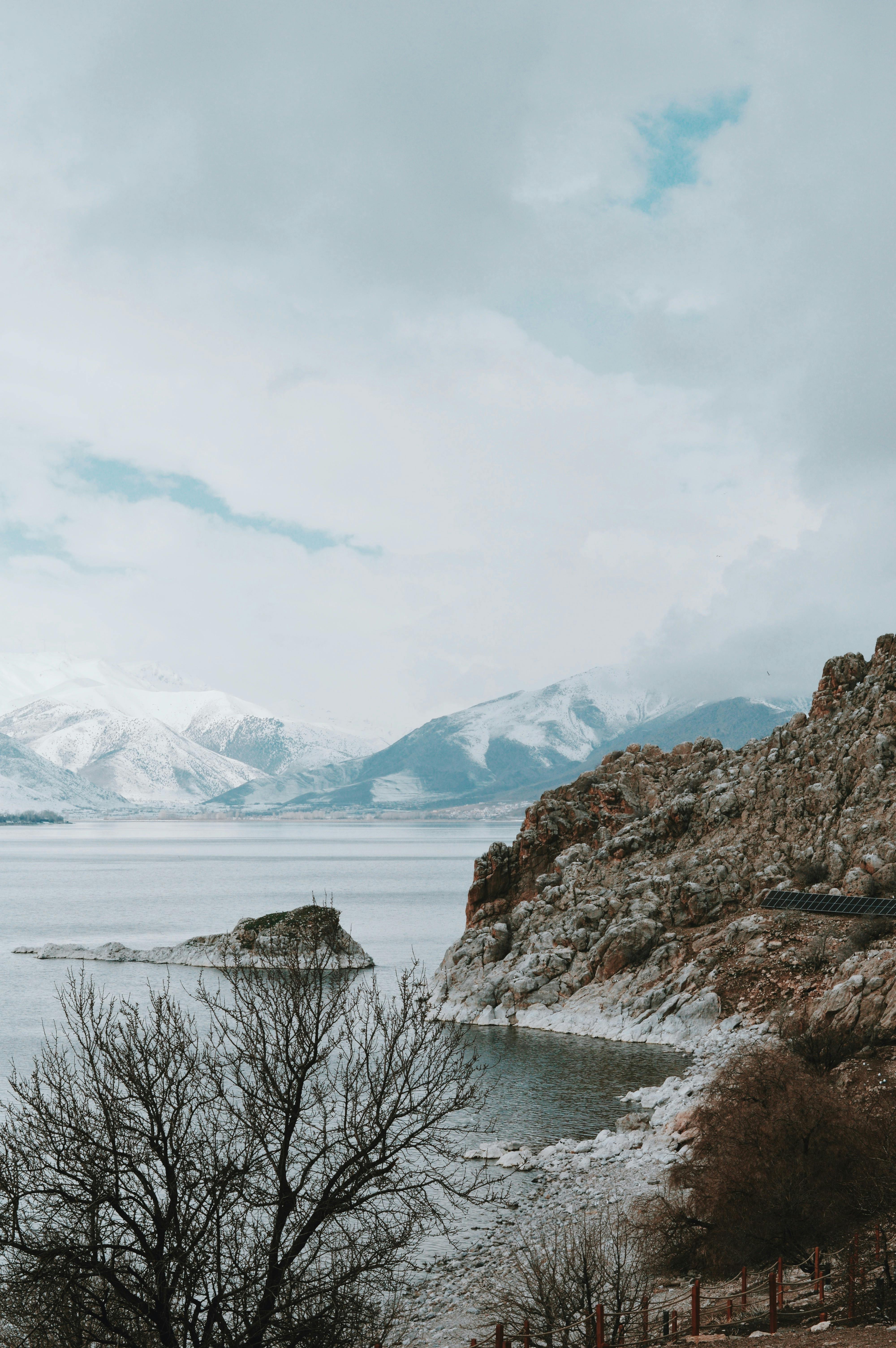 Scenic view of snow-capped mountains and rocky shorelines against cloudy skies, perfect for nature themes.