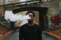 一位年轻时尚人士在涂鸦覆盖的桥下吸烟的肖像，为城市增添了气息