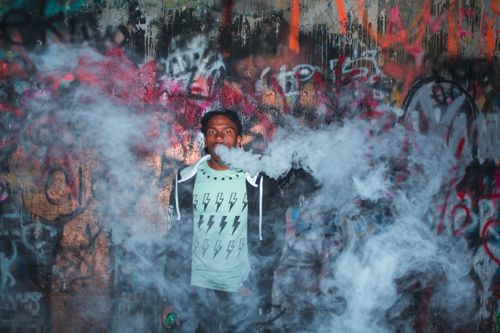 Free Dramatic urban portrait featuring a young man enveloped in smoke against a vibrant graffiti backdrop. Stock Photo