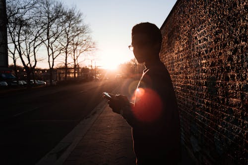 Free Boy Standing Near Wall Holding Smartphone While Looking Sideways Stock Photo