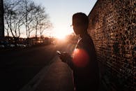 日落时分，一名男子在砖墙上使用手机的剪影令人惊叹，捕捉了城市生活的瞬间