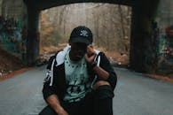 一张城市照片中，一名年轻黑人随意摆姿势于涂鸦覆盖的桥下