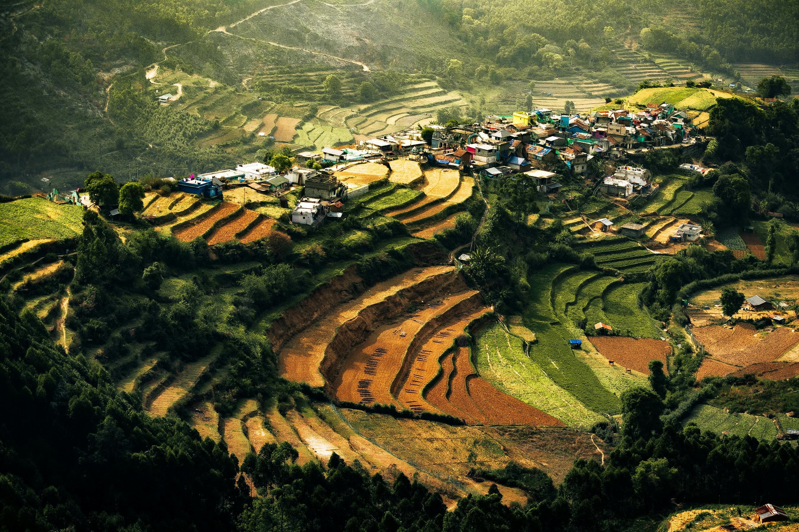 Scenic aerial shot of terraced fields and a vibrant village nestled in lush hills in sunlight.