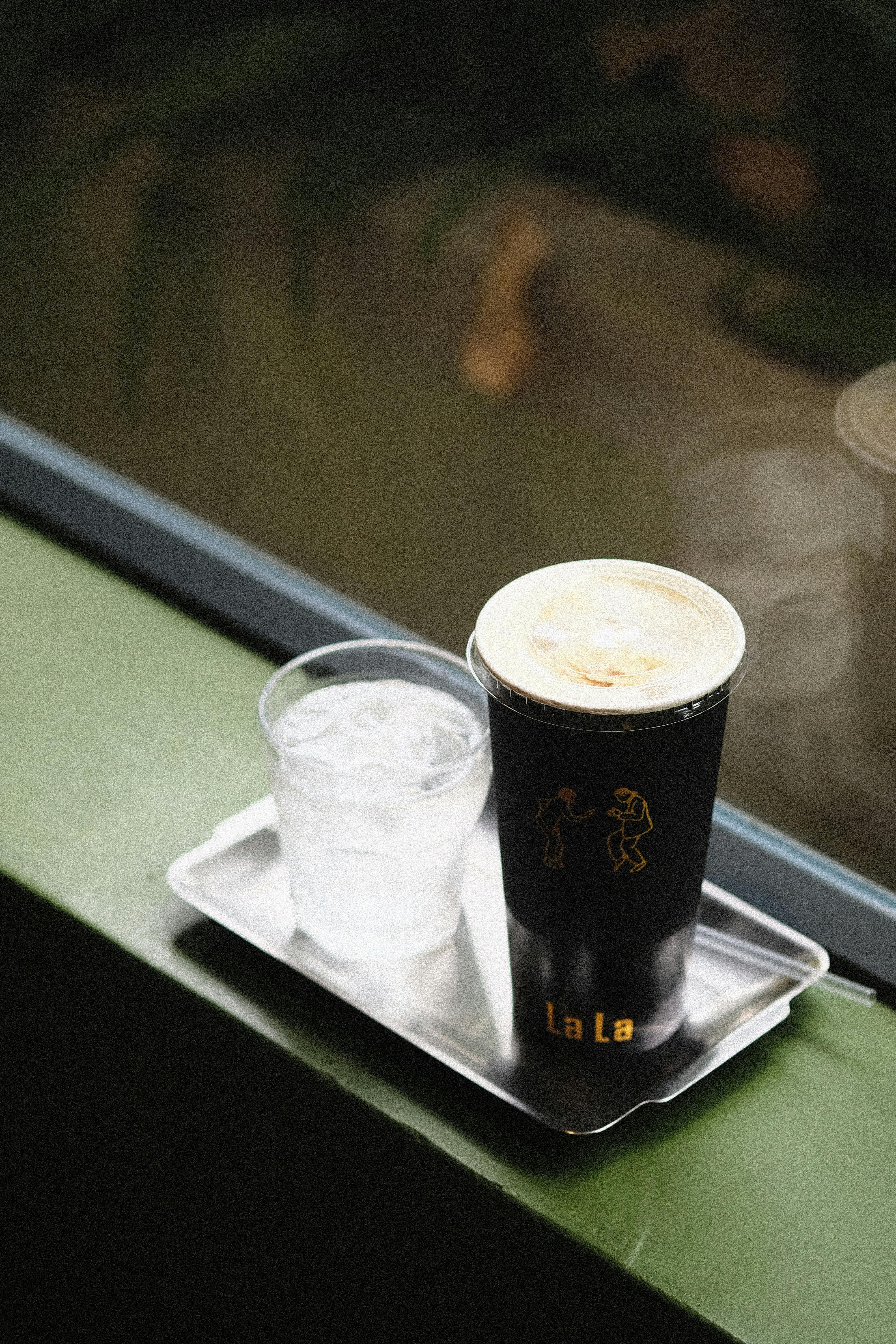 A stylish café scene with iced coffee and water glasses on a tray by a windowsill.