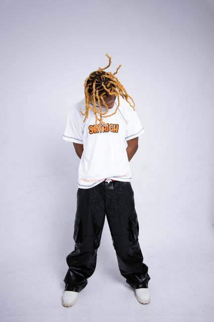 Model with dreadlocks poses in a white t-shirt and pants against a white background.