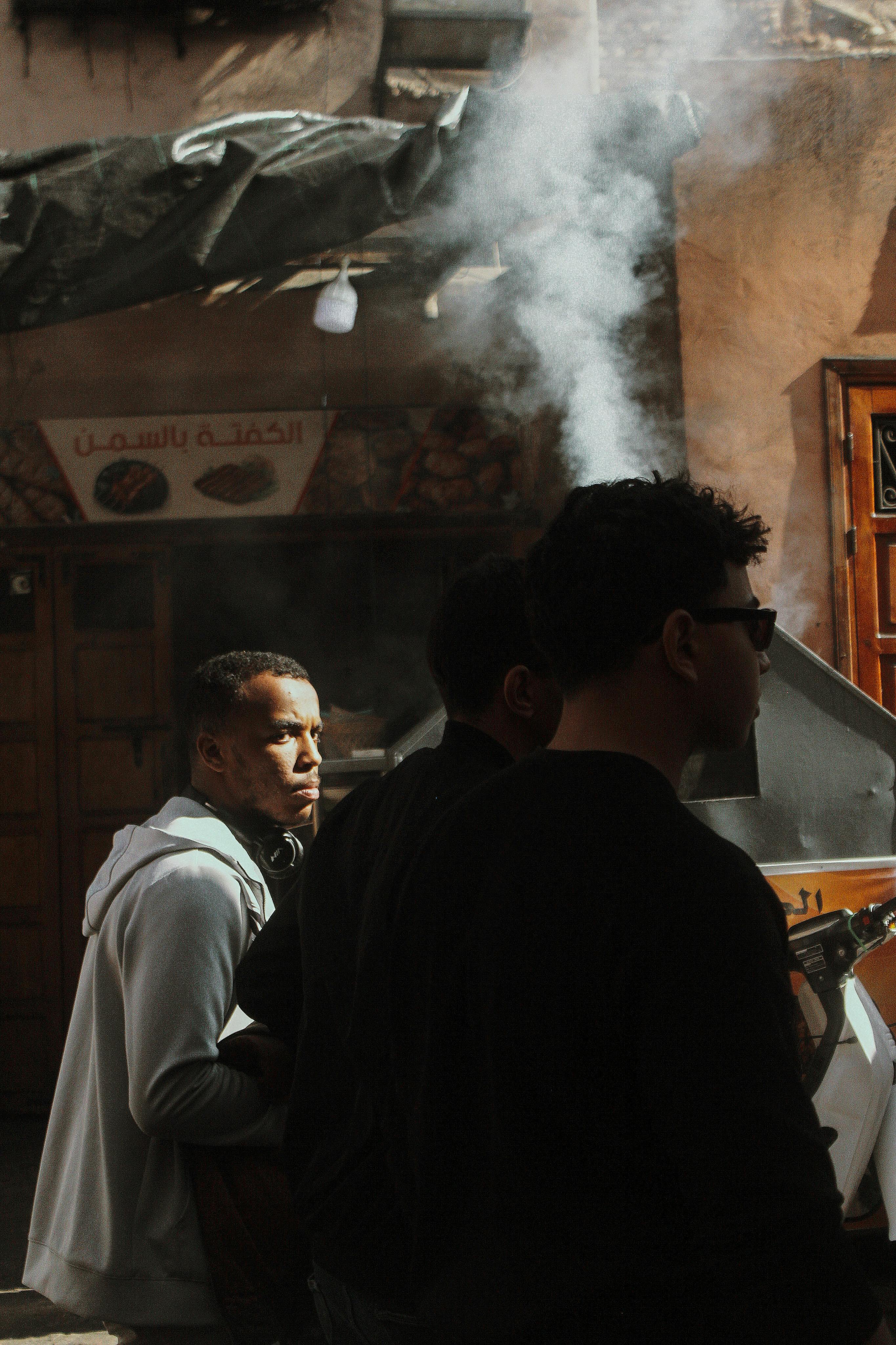 Men walking by a smoking food stand in a vibrant urban setting with wall art.