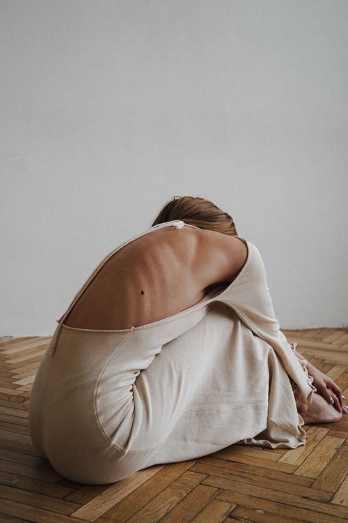 Free Back view of a woman in a beige dress sitting gracefully on a wooden floor. Stock Photo