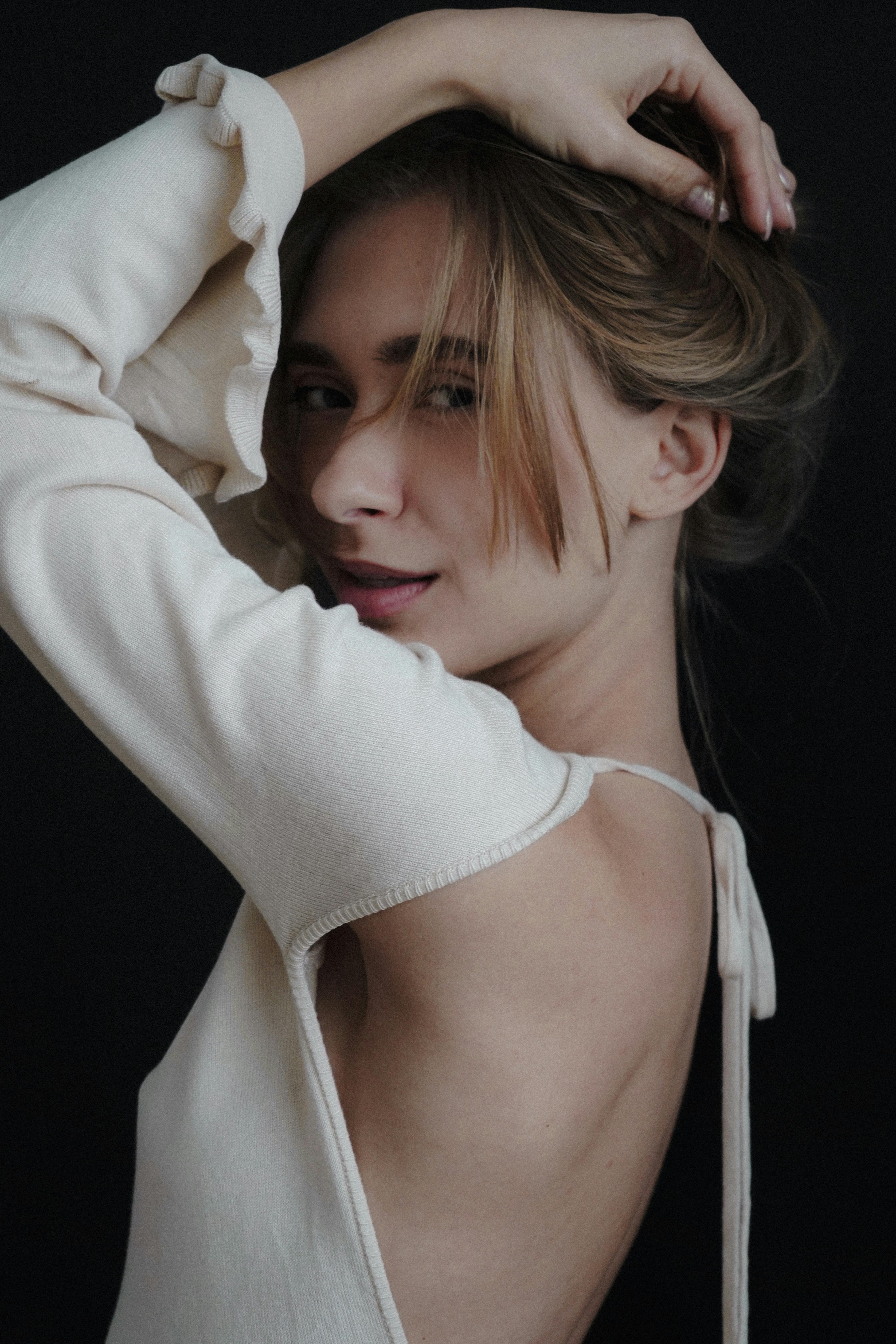Stylish young woman in an open back dress poses gracefully in a studio setting.