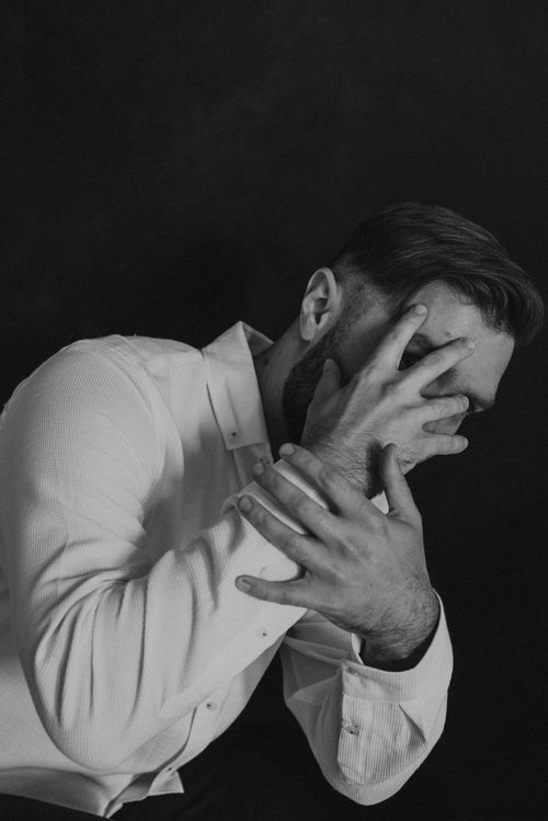 Free Emotive black and white portrait of a man covering his face in a studio setting. Stock Photo