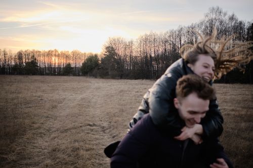 Free Joyful couple enjoying a playful moment in a rural field during sunset. Stock Photo