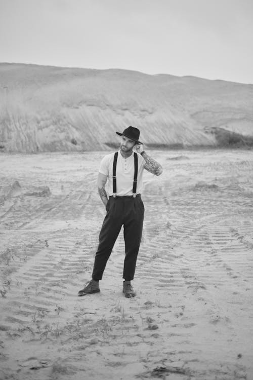 A man in suspenders and hat standing in the desert