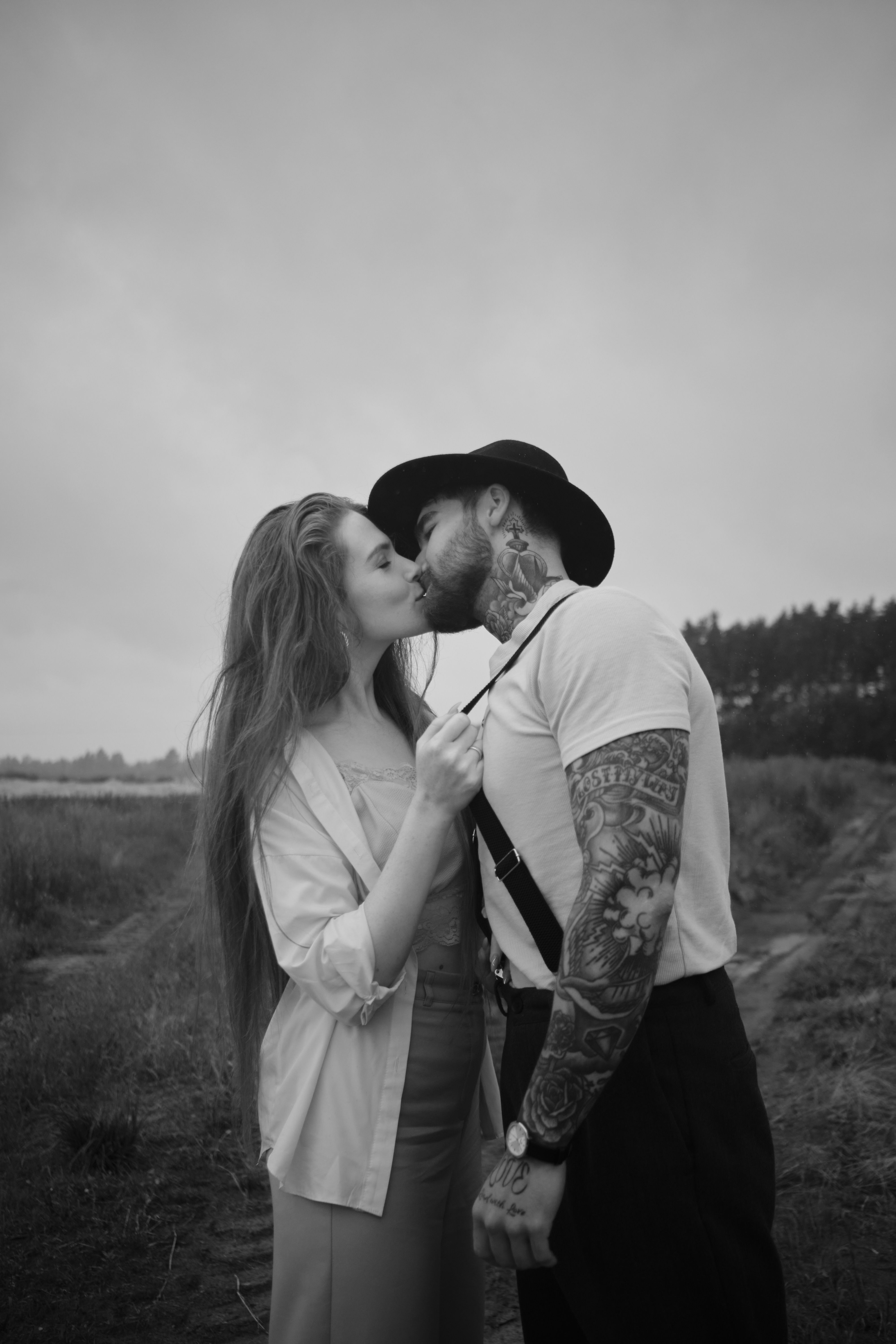 A stylish couple kisses outdoors in a black and white portrait.