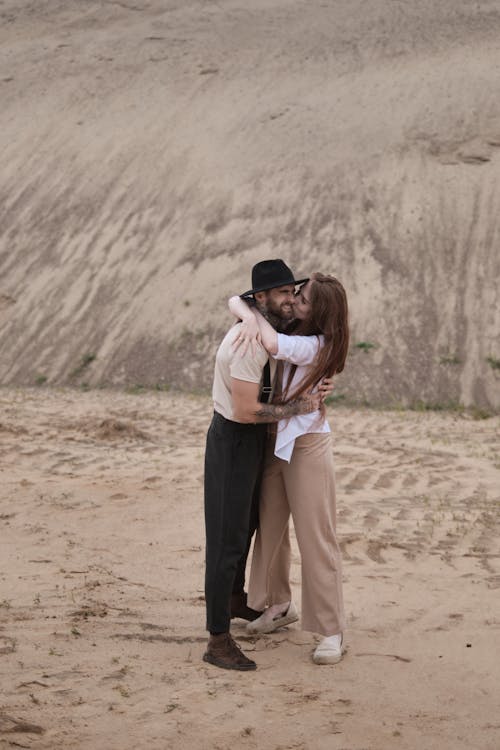 Two people hugging on the beach in front of a sand dune