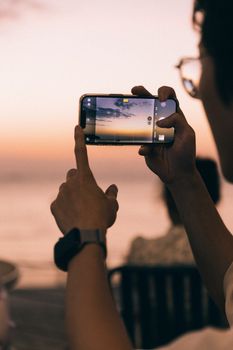 Person photographing a beautiful sunset at Langkawi beach using a smartphone.