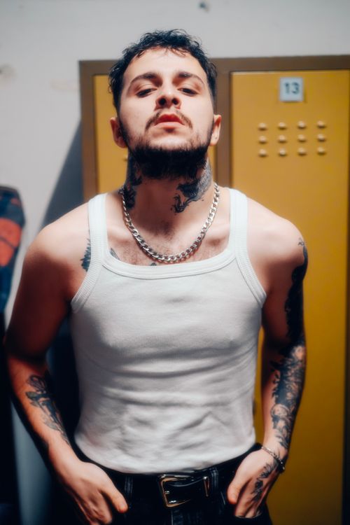 Free Portrait of a confident man with tattoos wearing a white tank top and chain necklace. Stock Photo