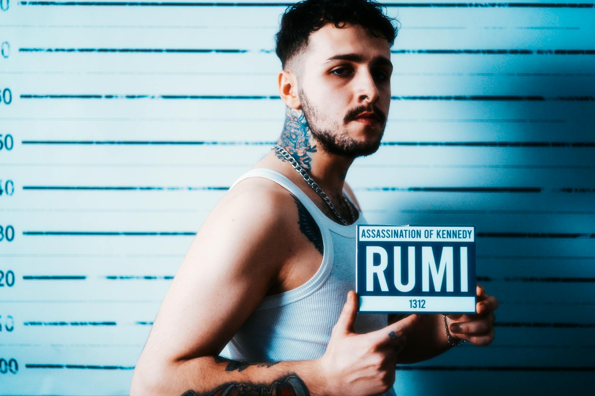 Man with tattoos posing in front of height chart holding a sign. Conceptual photography.