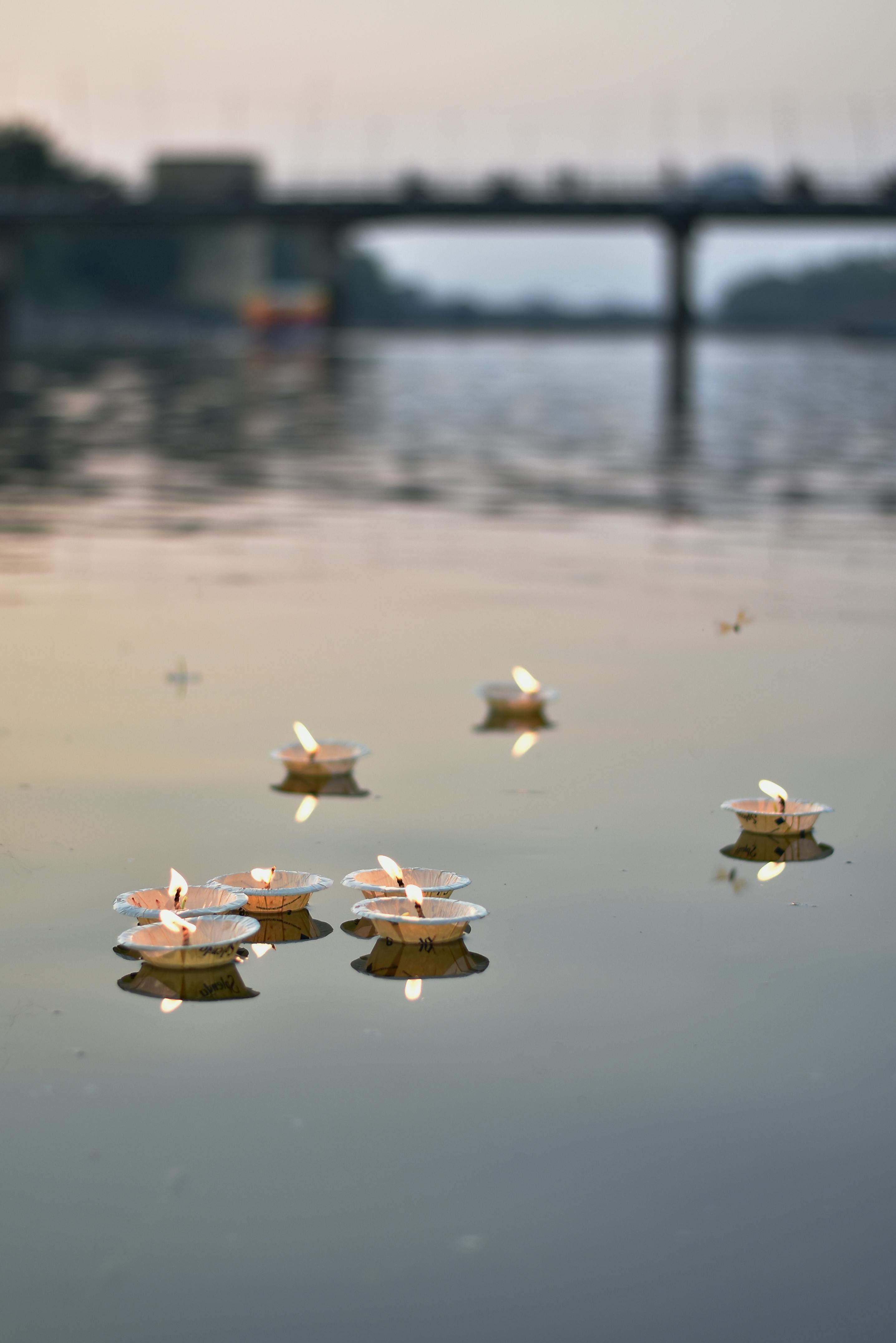 Floating candle lamps on a tranquil river with a serene bridge backdrop at dusk in Raipur, India.