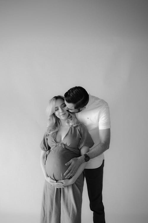 A pregnant woman is kissing her husband in black and white