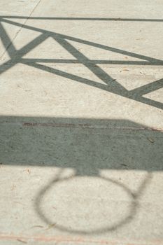 Abstract shadow of a basketball hoop on a concrete court, captured in an urban setting.