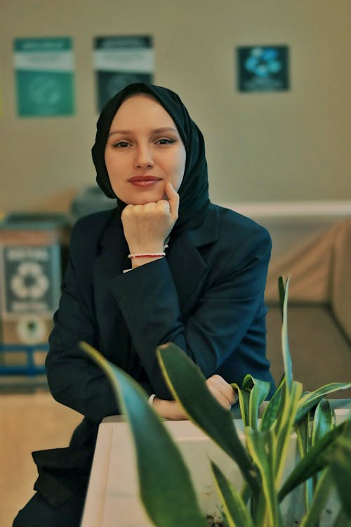 A woman in a hijab sitting in front of a plant