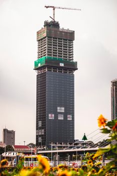 A tall skyscraper under construction with a crane against the city backdrop.