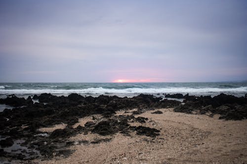 A sunset over the ocean with rocks and sand