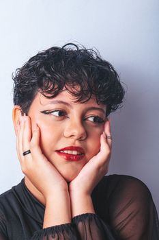 Studio portrait of a young woman with short curly hair, red lips, and black top, posing thoughtfully.