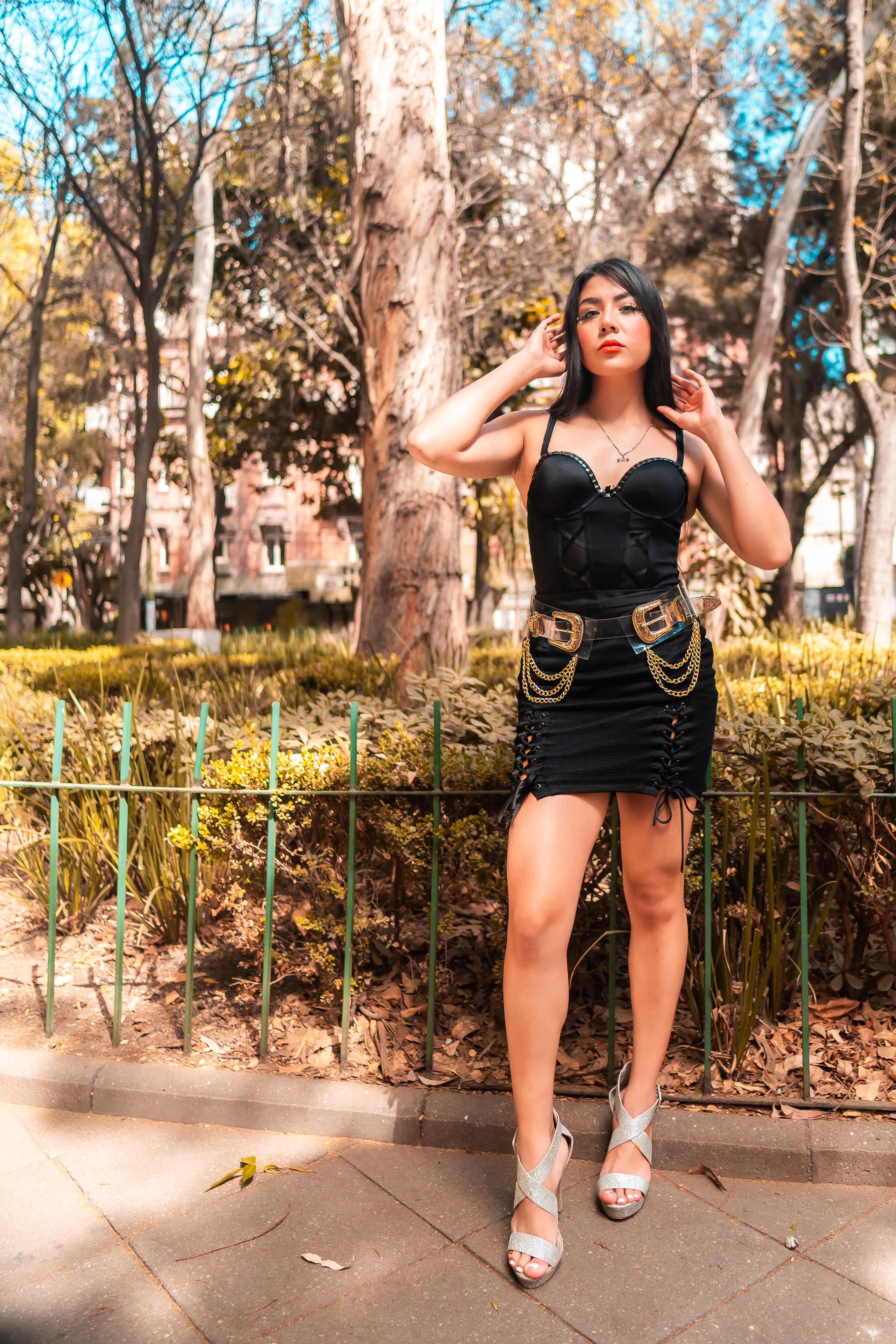 Fashionable woman in a black dress posing in a sunlit park in Mexico City.