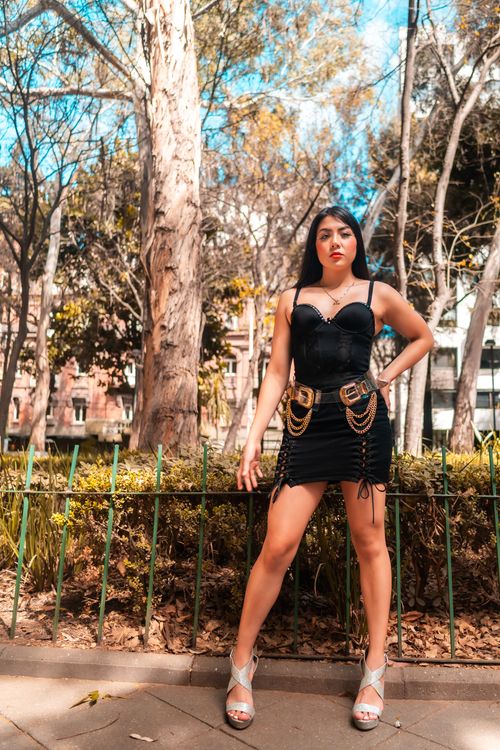 Free Fashionable woman in black dress posing confidently in a sunny urban park in Mexico City. Stock Photo