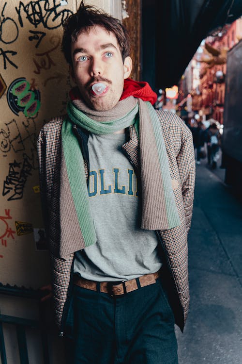 A man with a mustache and scarf standing in front of graffiti