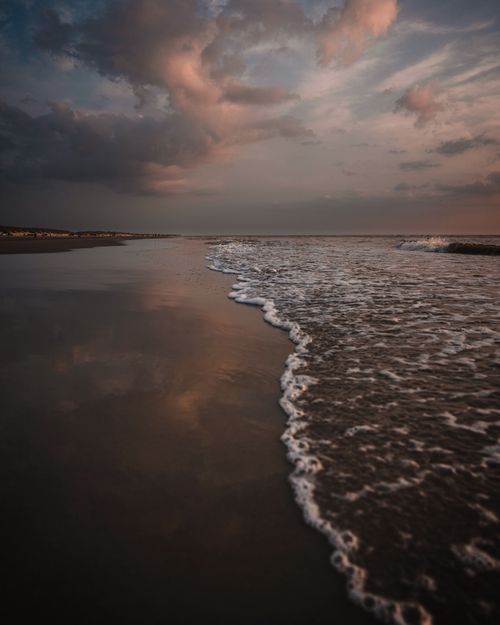 Free Serene beach scene at dusk with gentle waves and a dramatic sky reflecting on wet sand. Stock Photo
